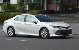 A white used Toyota Camry sedan parked on a city street, a popular choice for buyers looking for a reliable commuter car.
