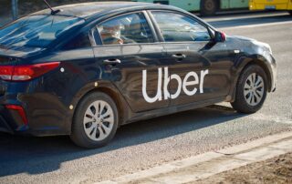 A black used sedan with a white Uber logo on the door driving on the street, highlighting the best pre-owned cars for rideshare and gig drivers.