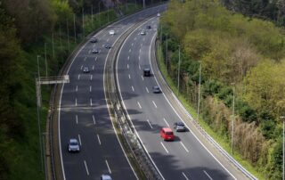 High-angle view of cars driving on a multi-lane highway surrounded by green trees, illustrating the daily commute and the importance of finding a fuel-efficient used car.