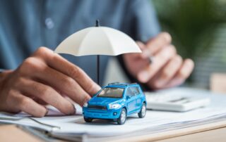 Insurance agent demonstrating car protection coverage with a miniature umbrella over a toy blue SUV.