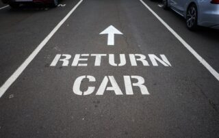 Painted RETURN CAR sign and directional arrow on asphalt in a vehicle rental drop-off lane.